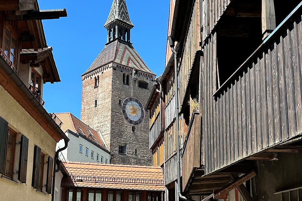 Das Foto von Robert Klinger zeigt den Schmalzturm (Schöner Turm) im Hexenviertel von Landsberg am Lech mit Fachwerkhäusern und Holzbalkonen im sonnigen Altstadtbild.
