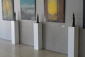 Abstrakte Gemälde in Gelb, Blau und Schwarz auf grauen Wänden im Rathausfoyer Landsberg am Lech: Skulpturen auf Sockeln, Pflanzenkübel und helle Galerie mit bodentiefen Fenstern.