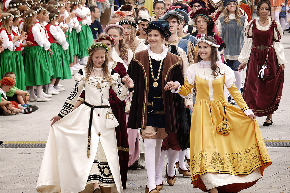 Bunte historische Kostüme beim Ruethenfest-Einzug Landsberg: Mädchen in grünen Trachten und Jungen in Ritterkleidern laufen Händchen haltend über den Platz.