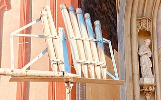 Große, silbern-blaue Orgelpfeifen ragen in der gotischen Stadtkirche Mariä Himmelfahrt empor, neben einer Statue eines Heiligen – Detail zum Landsberger Orgelsommer.