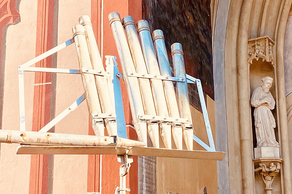 Große, silbern-blaue Orgelpfeifen ragen in der gotischen Stadtkirche Mariä Himmelfahrt empor, neben einer Statue eines Heiligen – Detail zum Landsberger Orgelsommer.