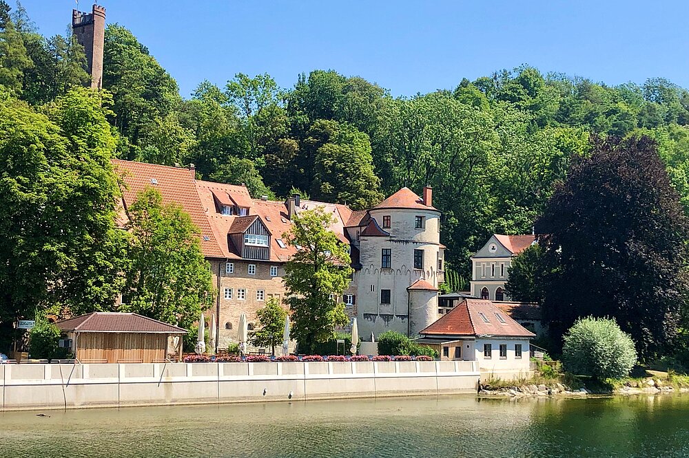 Idyllische Ansicht des Klösterls mit Nonnenturm in Landsberg am Lech am Lech-Ufer, umgeben von grünen Bäumen und sonnigem Himmel, CC-BY-SA.