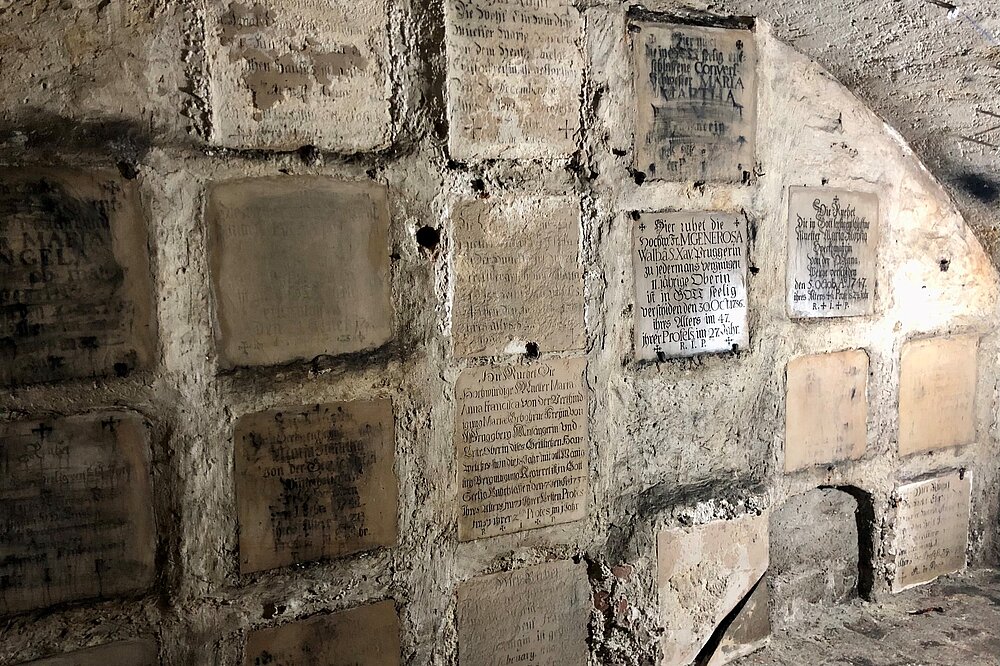 Dunkle Gewölbe der Ursulinengruft Landsberg mit historischen Grabplatten und Inschriften an den Steinwänden.