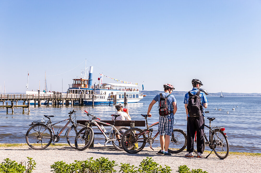 Wanderer mit Rucksack steht am Kneippbecken mit klarem Wasserbecken und Fußbad in der Natur des Wildparks Pössinger Au Landsberg am Lech – Wandern Lechpark Bayern mit Wellness (CC BY-SA Klinger)
