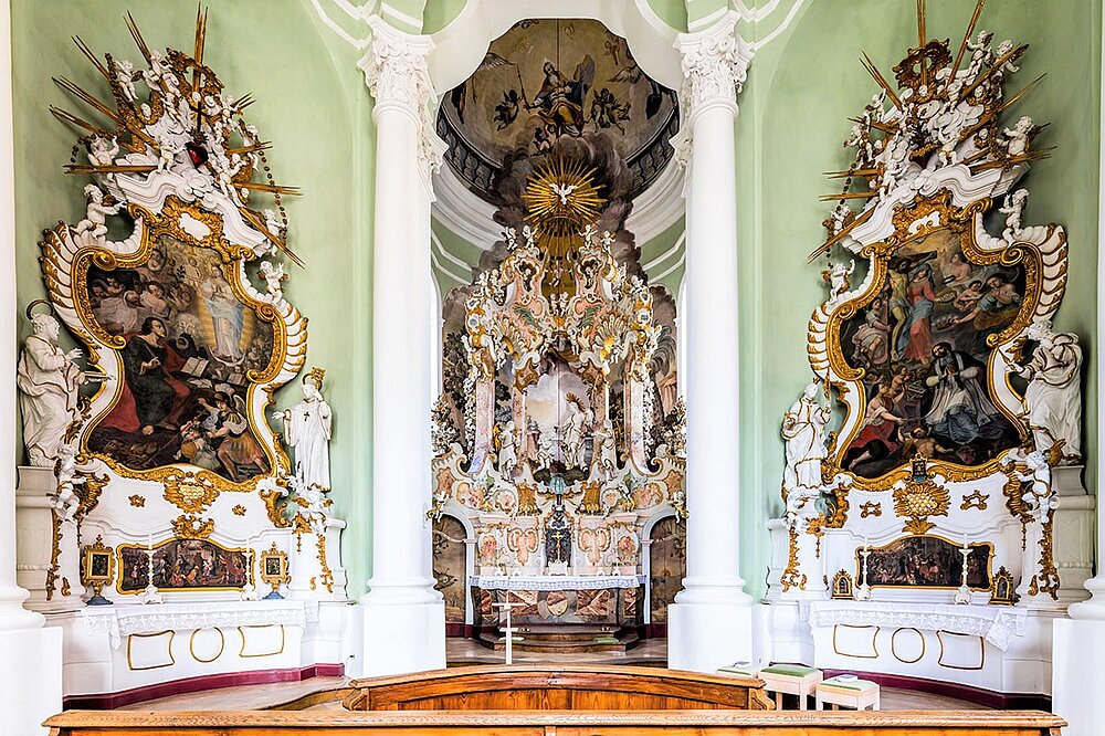 Rokoko‑Hochaltar der Johanniskirche Landsberg mit üppigem Stuck, Fresken, Statuen und grünem Raum vor goldenem Altar.