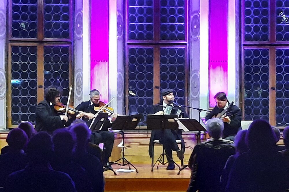 Quartett mit Violine, Geige, Drehleier und Akkordeon performt im Rathauskonzert Landsberg: Lila beleuchtete Fenster, Notenständer und konzentriertes Publikum.
